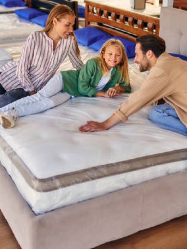 A young family with their lovely daughter lay down on the bed, trying the mattress for softness in the store. Buying a bed and bedding.